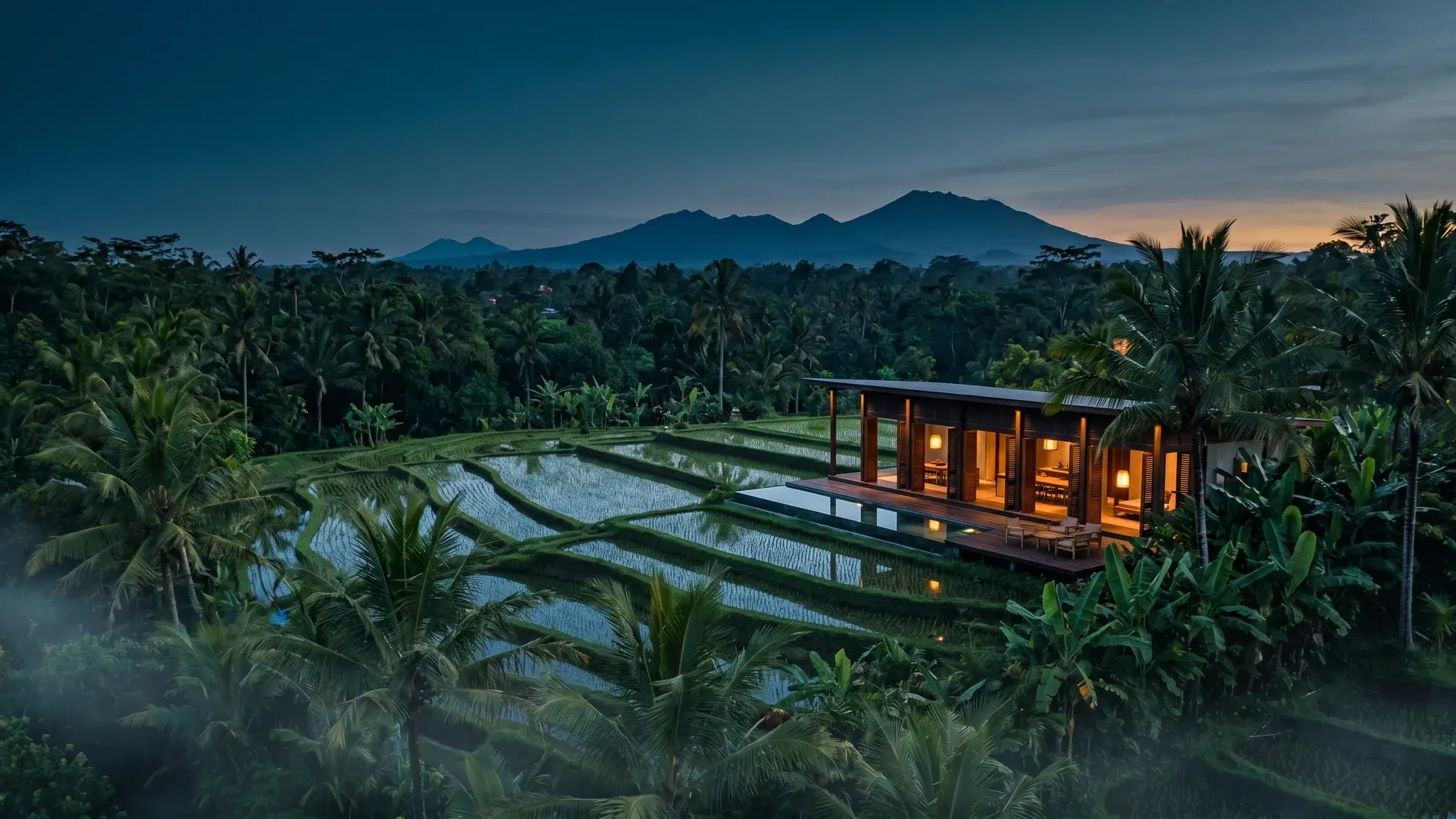 Editorial twilight aerial — Tjampuhan ridge, terraced paddies, modernist villa, distant Mount Batur silhouette