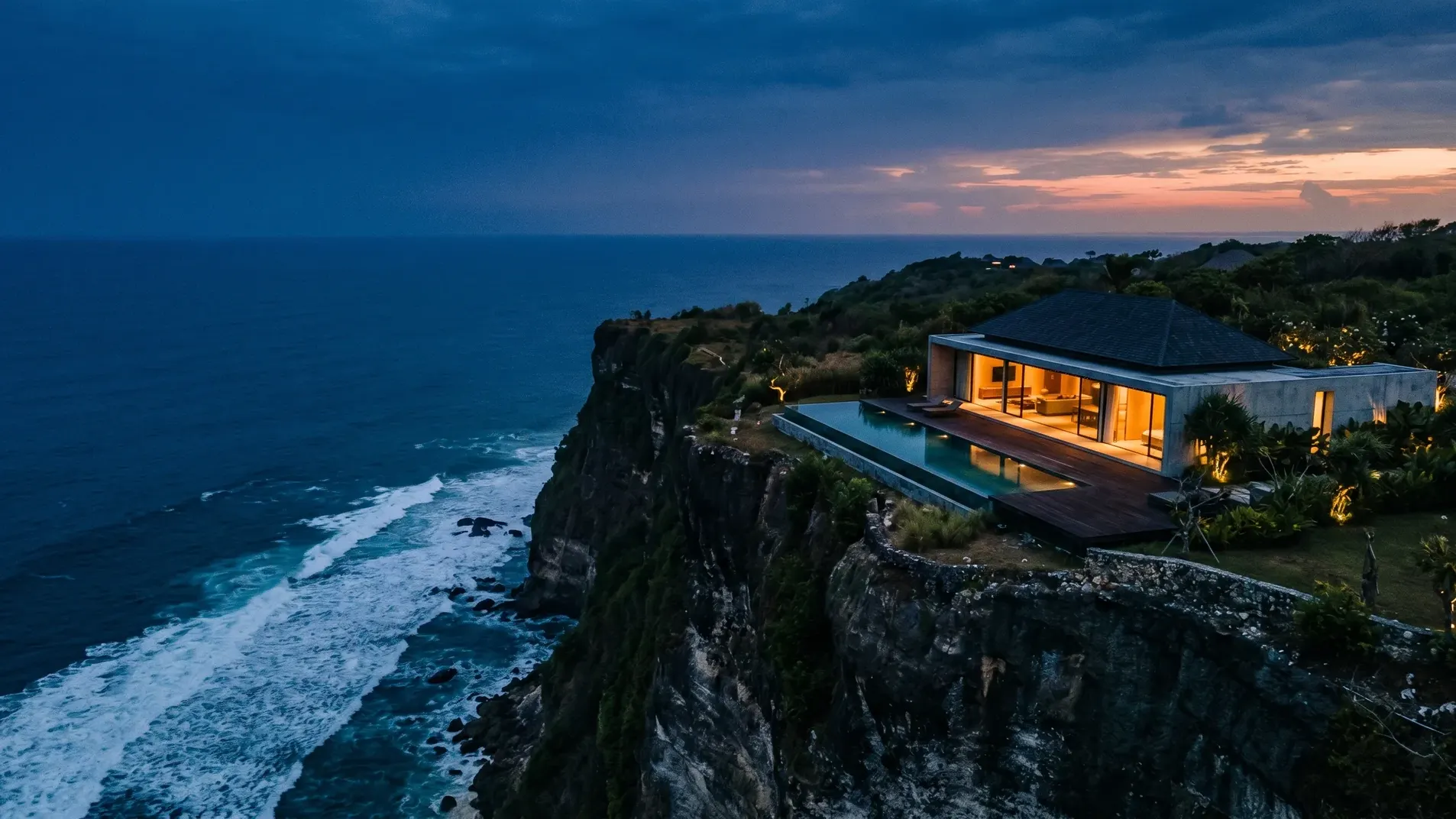 Redaktionelle Luftaufnahme einer Uluwatu-Klippen-Villa, freitragend über Kalkstein-Karst in der Dämmerung, Infinity-Pool spiegelt den kobaltblauen Himmel