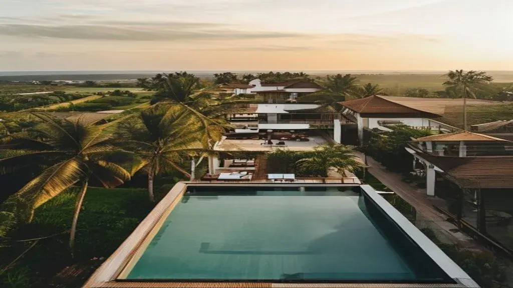 Editorial aerial view of a modern Canggu villa compound at golden hour, rice paddies in the distance, palm-lined streets with scooters